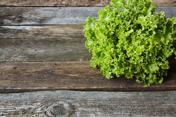 Head of green fresh salad with root on an old rough wooden surface, healthy eating concept, selective focus - Photo, Image