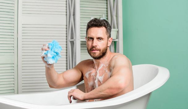 Treating yourself with hot bath. Pampering and beauty routine. Man handsome muscular guy relaxing in bathtub. Macho with sponge take bath at home. Metrosexual concept. Taking bath with soap suds - Photo, Image