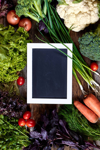 Świeże warzywa i zioła na starej, szorstkiej drewnianej powierzchni i kredą do napisu lub menu, koncepcja zdrowego odżywiania, selektywna koncentracja - Zdjęcie, obraz