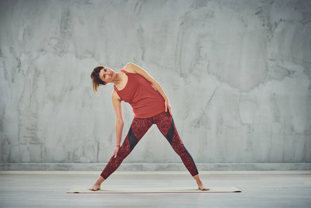 Attractive brunette in red sportswear barefoot doing Triangle yoga posture. - Φωτογραφία, εικόνα