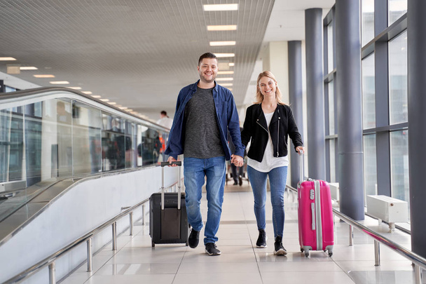 Image of walking happy man and woman walking along walkway with suitcases at airport . - Foto, Bild