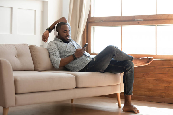 Black man relaxing on sofa at home, listen music. - Zdjęcie, obraz