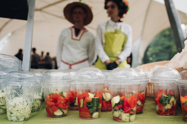Verduras orgánicas en tazas para llevar Primer plano de un montón de tazas de plástico llenas de verduras picadas y ensaladas en la mesa en el festival de alimentos. Ensalada para llevar y verduras en la mesa
. - Foto, Imagen