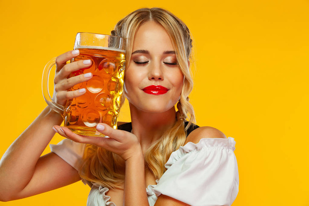 Young sexy Oktoberfest girl waitress, wearing a traditional Bavarian or german dirndl with big beer mug isolated on yellow background. Woman love beer. - Foto, Bild