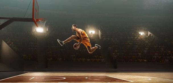 アクションでバケトボールプレーヤー。かごを作るレイアップショット。フラッドライトバスケットボールコート - 写真・画像