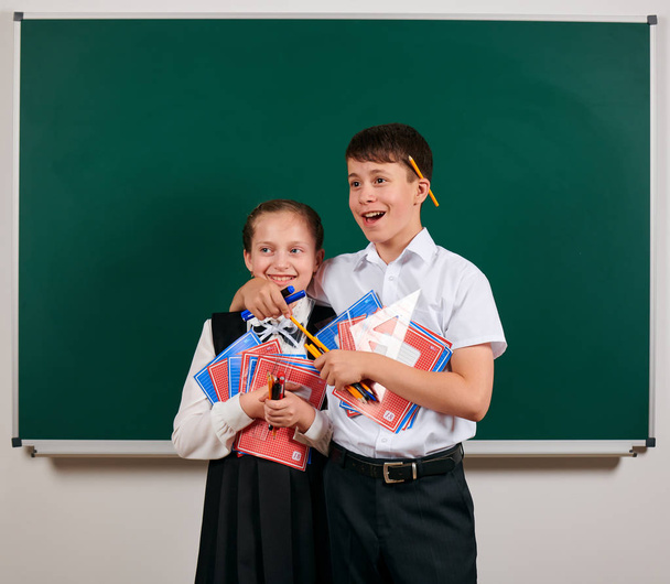 Емоційний портрет школяра і школярки, що позує з тренажерами, ручками, олівцями та іншими шкільними приладдям на фоні дошки назад до школи та концепції освіти
 - Фото, зображення