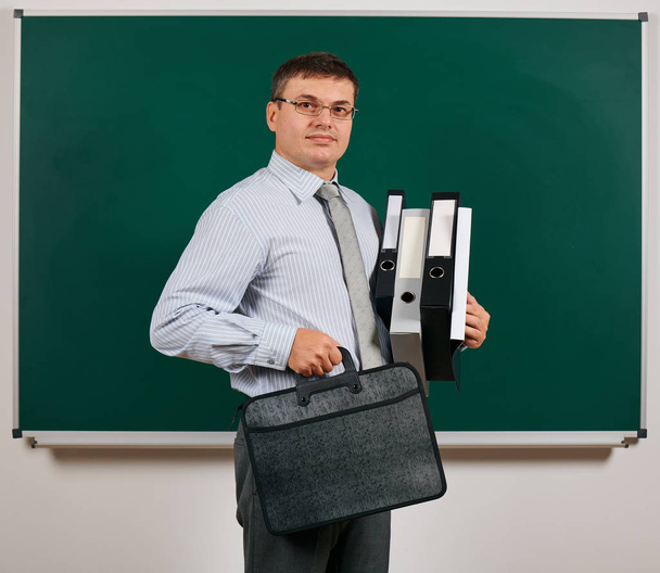 Retrato de um homem vestido em terno de negócios com pastas, documentos e pasta, posando em fundo de quadro-negro - conceito de aprendizagem e educação
 - Foto, Imagem