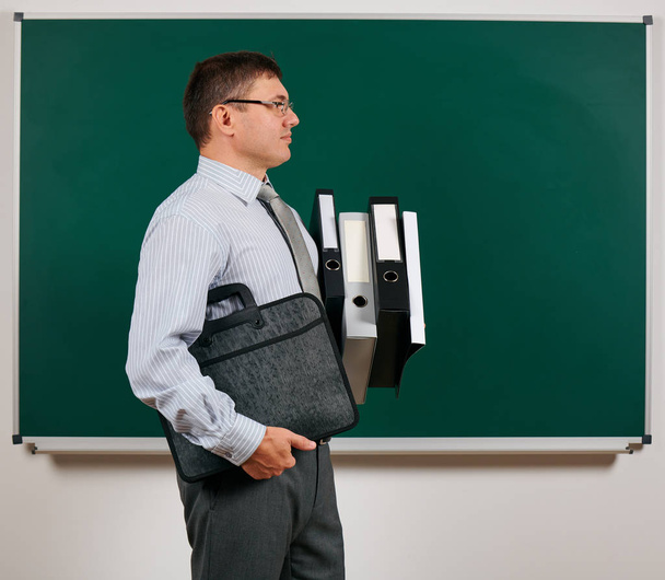Portrait of a men dressed in business suit with folders, documents and briefcase, posing at blackboard background - learning and education concept - Photo, Image