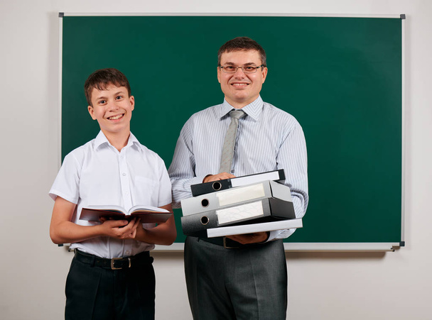 Portret van een leraar gekleed in Business Suit met mappen, documenten, poseren met school jongen op Blackboard achtergrond-Learning and education concept - Foto, afbeelding