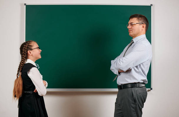 Πορτρέτο ενός δασκάλου και μαθήτρια, που ποζάρει στο φόντο του μαυροπίνακα-πίσω στο σχολείο και την εκπαίδευση έννοια - Φωτογραφία, εικόνα