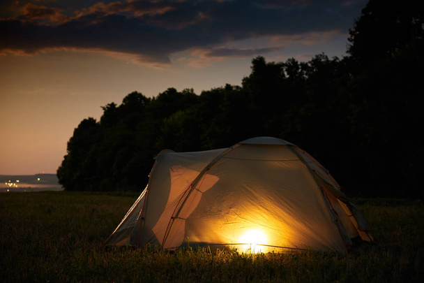 Concepto de viaje y camping - tienda de campaña en la noche bajo un cielo lleno de estrellas. Tienda iluminada naranja. Hermosa naturaleza - campo, bosque, llanura. Luna y luz de luna
 - Foto, Imagen
