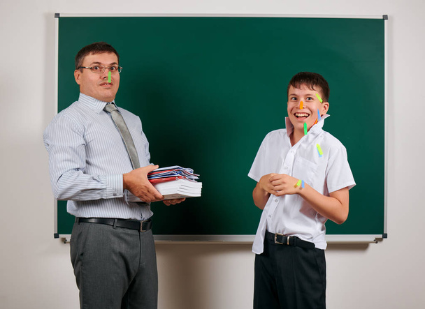 Portret van een leraar en grappige school jongen met lage discipline, slechte schoolprestaties, poseren op Blackboard achtergrond-terug naar school en onderwijsconcept - Foto, afbeelding