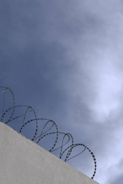 Concertina wire perimeter on a wall, silhouette against blue sky. Plenty of copy space. - Photo, Image