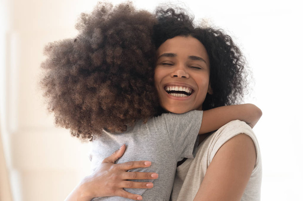 Happy excited single african american mother cuddling little preschool daughter. - Foto, afbeelding