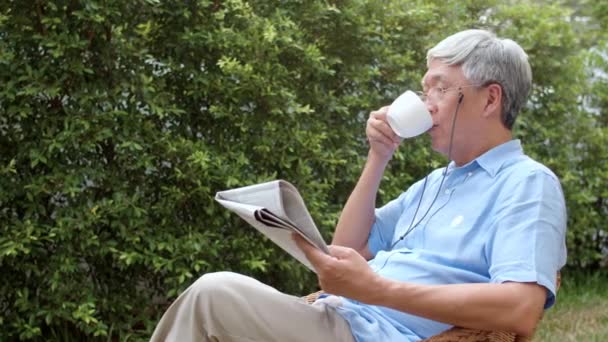 Gli uomini anziani asiatici si rilassano a casa. asiatico anziano cinese maschio godere di riposo tempo indossare occhiali leggere giornale e bere caffè mentre sdraiato in giardino a casa in il mattina concetto. - Filmati, video