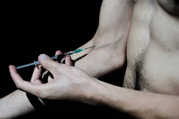 Man injecting intravenous drug. Dark studio shot. - Foto, Imagem
