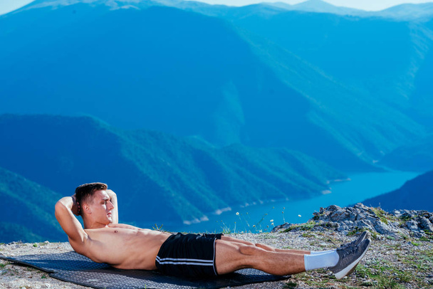 Een sterke fit mannelijke atleet heeft een buiktraining op de top van een berg. - Foto, afbeelding