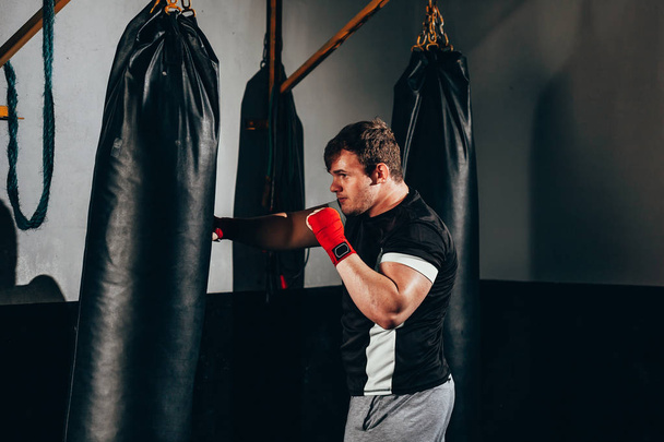 Muscular kickbox fighter exercising with punch bag at the gym - Foto, afbeelding