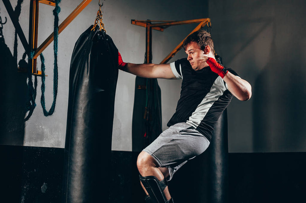 Muscular kickbox fighter exercising with punch bag at the gym - Valokuva, kuva