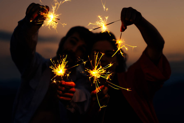 Концепция вечеринки, мероприятия и праздника - мужчина и женщина с искрами на фоне закатного неба
 - Фото, изображение