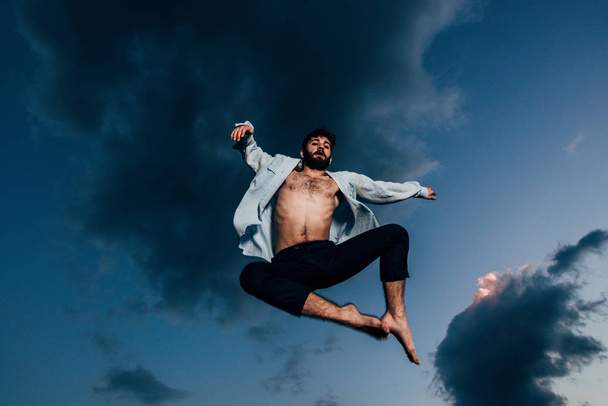 Όμορφος νέος χορευτής που εκτελεί μοντέρνο χορό πάνω από τον γαλάζιο ουρανό - Φωτογραφία, εικόνα
