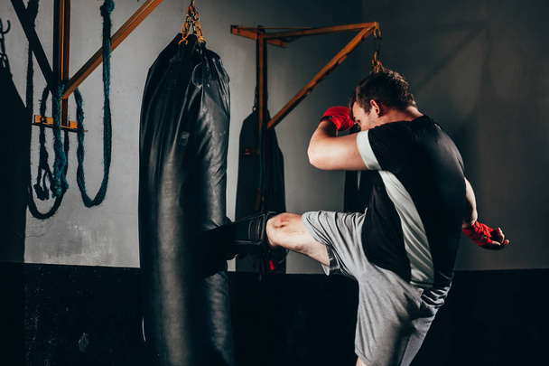 Muscular kickbox fighter exercising with punch bag at the gym - Photo, image