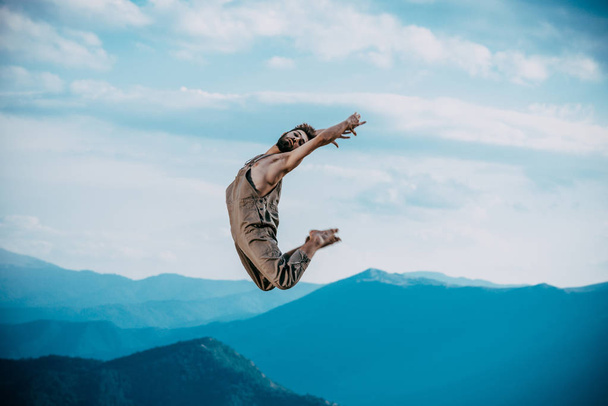 Profilansicht einer männlichen urbanen Tänzerin, die ein paar Tanzschritte übt und im Freien springt - Foto, Bild