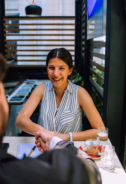 Lächelnde junge Frau beim Händeschütteln mit einem Versicherungsvertreter oder Anlageberater, während er in einem Meeting sitzt - Foto, Bild