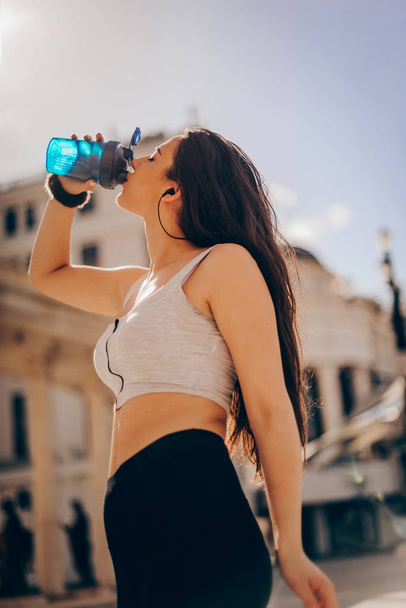 Young beautiful athlete drinking water after exercising to revitalize - Foto, Imagem