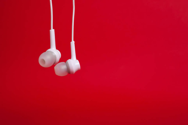 Écouteurs suspendus blancs (écouteurs) sur un fond rouge avec copyspace
 - Photo, image