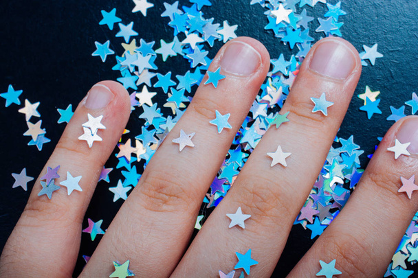 Hand op kleurrijke confetti sterren op een donkere kleur achtergrond - Foto, afbeelding
