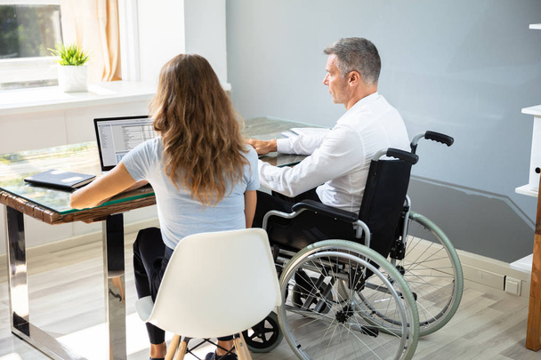 Disabled Businessman Sitting With His Partner With Laptop Over Desk In Office - Foto, imagen