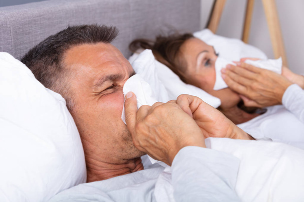 Sick Mature Couple Lying On Bed Blowing Their Nose In Bedroom - Fotoğraf, Görsel
