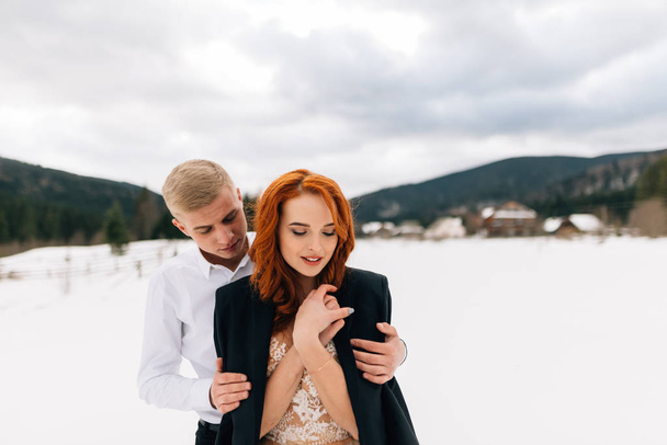 casamento no inverno, um jovem homem elegante abraça uma noiva bonita e terna. Menina com cabelo vermelho
. - Foto, Imagem