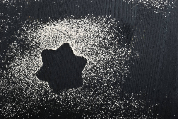 The dark wooden surface is sprinkled with flour. On flour, a trace in the form of an asterisk. View from above. Close-up. Macro photography. - Foto, afbeelding