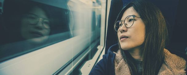 Banner of webpagina van Aziatische jonge dame passagier zittend in depressieve stemming naast het raam binnen trein die reizen tussen de stad wanneer reizen alleen voor ontsnappen aan de chaos, reiziger en druk concept - Foto, afbeelding