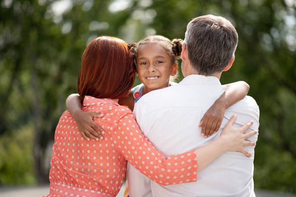 Dark-skinned girl feeling happy while hugging her foster parents - Фото, зображення