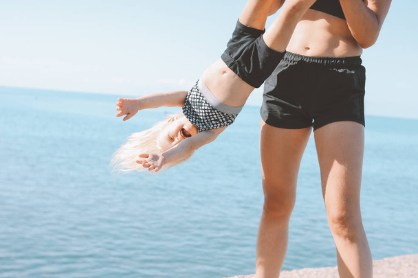 Young fit woman mom with little cute girl exercising on beach together, healthy lifestyle, dynamic gymnastic - Foto, imagen