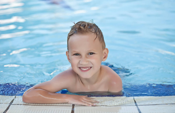Ευτυχισμένο αγόρι με ξανθά μαλλιά χαμογελώντας καθισμένος στην πισίνα - Φωτογραφία, εικόνα
