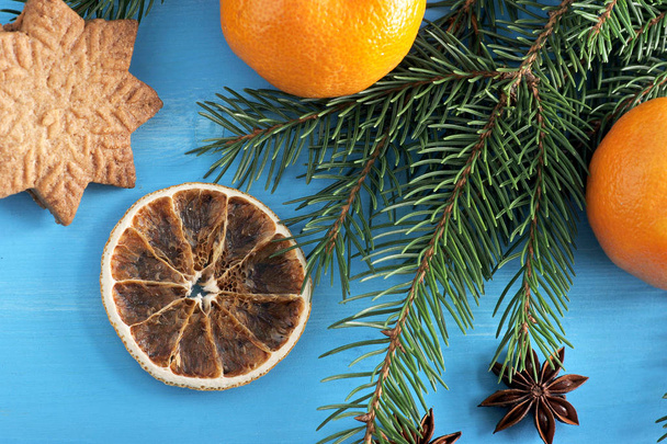 Christmas composition of spruce branches, mandarin, cookies, anise and slices of orange. Blue wood background. Close-up. View from above.  Macro photography. - Φωτογραφία, εικόνα