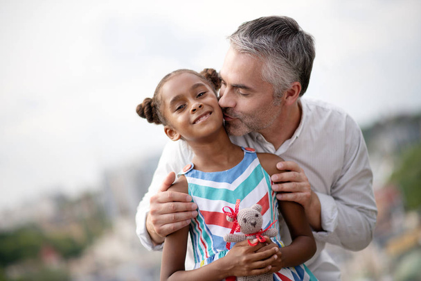 Grey-haired foster father kissing his cute dark-skinned daughter - Foto, afbeelding