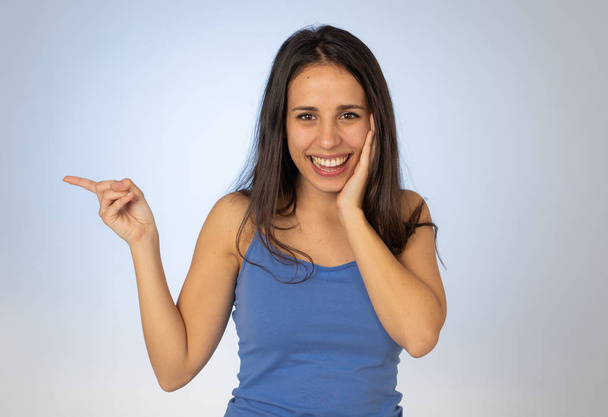 Beautiful latin young woman pointing finger at copy space looking cheerful happy and excited. Teenager girl showing something interesting isolated on empty background for text advertising content. - Fotó, kép