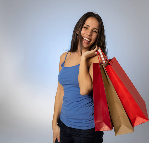 Happy latin young woman holding colorful bags happy and cheerful after a shopping day. Excited teenager with paper bags buying in new season sales. In fashion and and shopping addiction concept - Photo, image