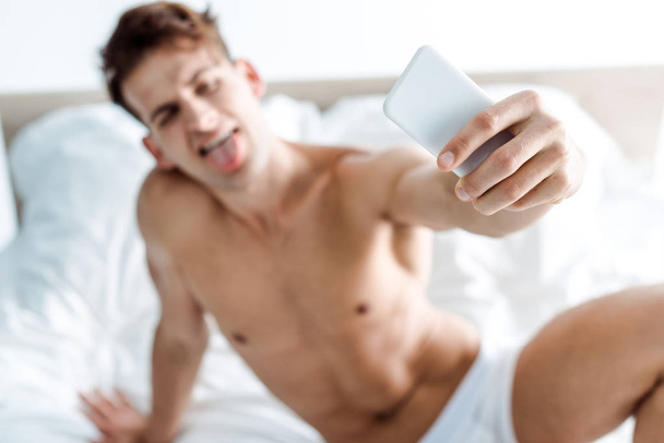 selective focus of sexy and shirtless man taking selfie in bedroom  - Фото, изображение