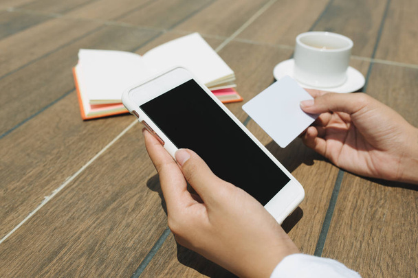 Fechar a mão mulher segurando cartão de crédito e telefone celular tela em branco sentado no café
 - Foto, Imagem