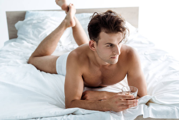 ベッドに横たわり、ウイスキーでグラスを持つセクシーな男の選択的な焦点  - 写真・画像