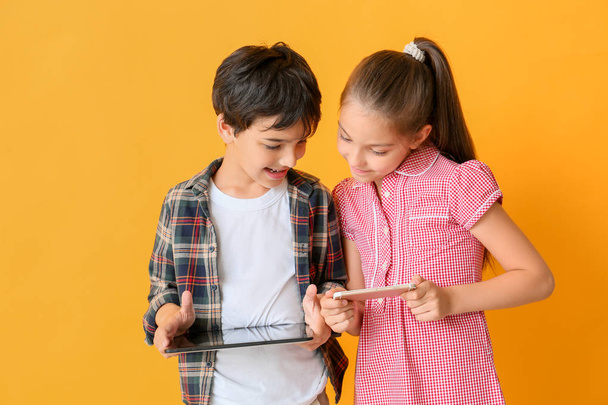 Cute little children with tablet computer and mobile phone on color background - Foto, afbeelding