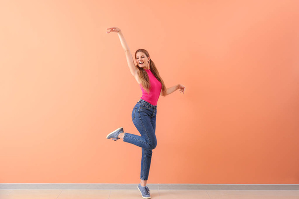 Beautiful young woman dancing against color wall - Foto, afbeelding