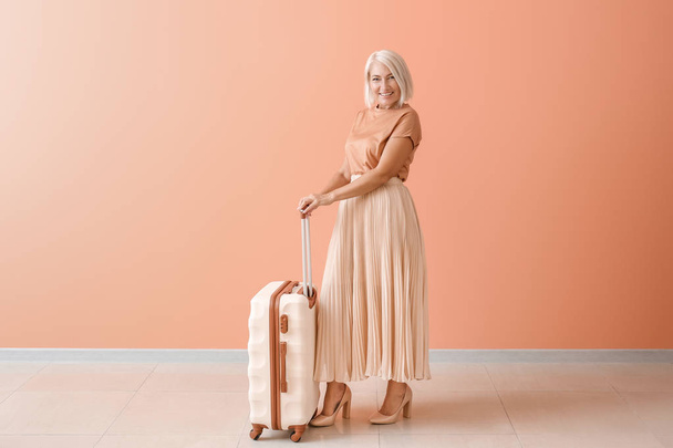 Mature woman with suitcase near color wall - Photo, Image