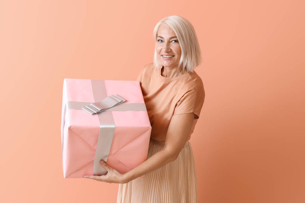 Зрелая женщина с подарочной коробкой на цветном фоне
 - Фото, изображение